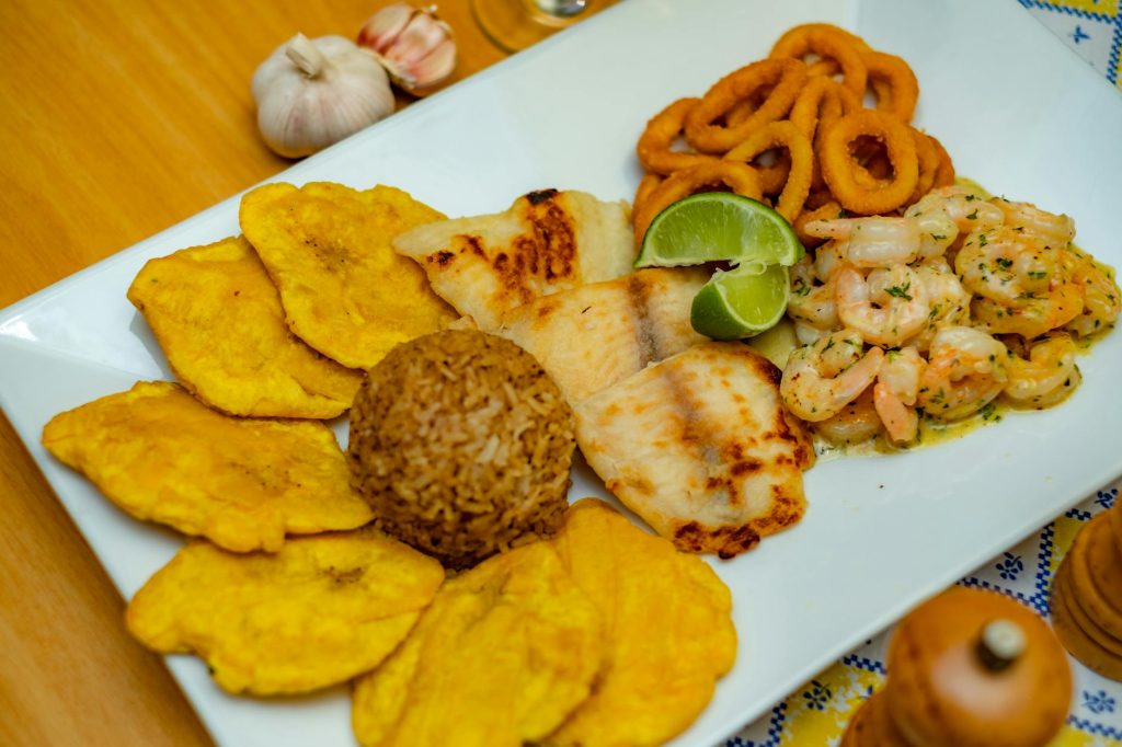 tostones rice prawns fish and onion rings on a plate